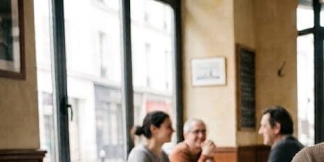 Trois clients attablés près de la baie vitrée d'une brasserie parisienne, l'ardoise du jour accrochée au mur.